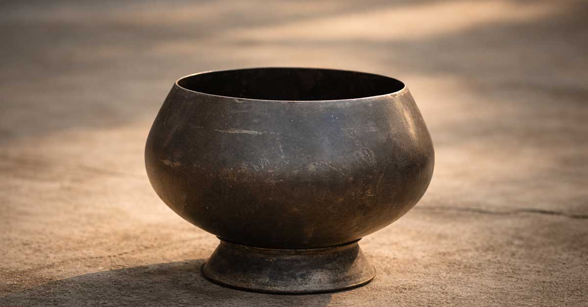begging-bowl-buddhist-mindfulness Worn metal Buddhist alms bowl resting on a stone surface in soft afternoon light