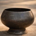 Worn metal Buddhist alms bowl resting on a stone surface in soft afternoon light