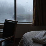 Dim early-morning hotel room with a chair by a foggy window, a phone, notebook, and folded martial arts uniform on the bed.