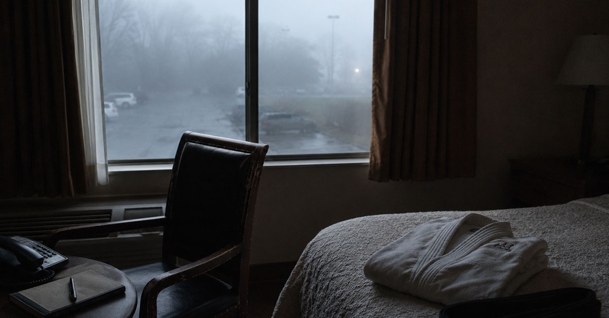 Dim early-morning hotel room with a chair by a foggy window, a phone, notebook, and folded martial arts uniform on the bed.